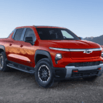 Red 2026 Chevy Silverado EV parked on rocky ground with desert hills and clear blue sky