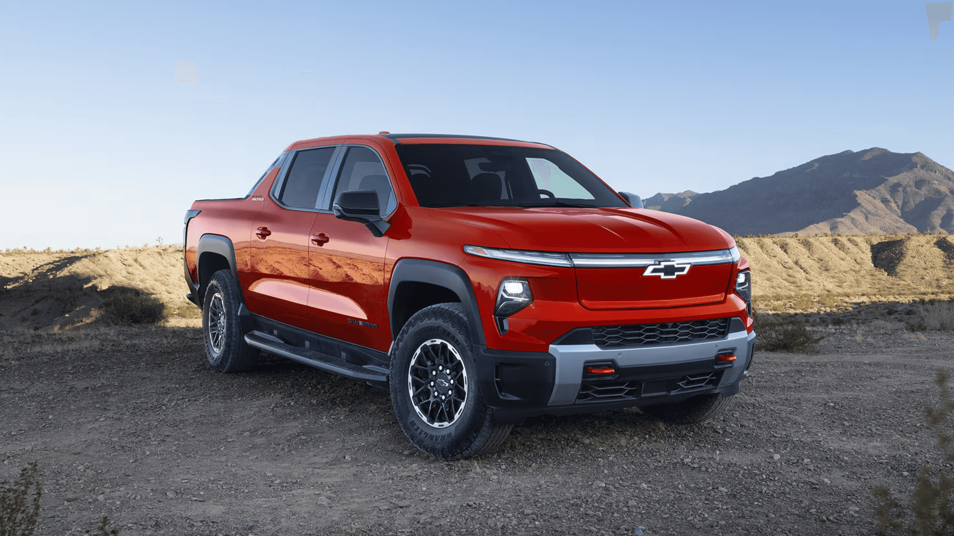 Red 2026 Chevy Silverado EV parked on rocky ground with desert hills and clear blue sky
