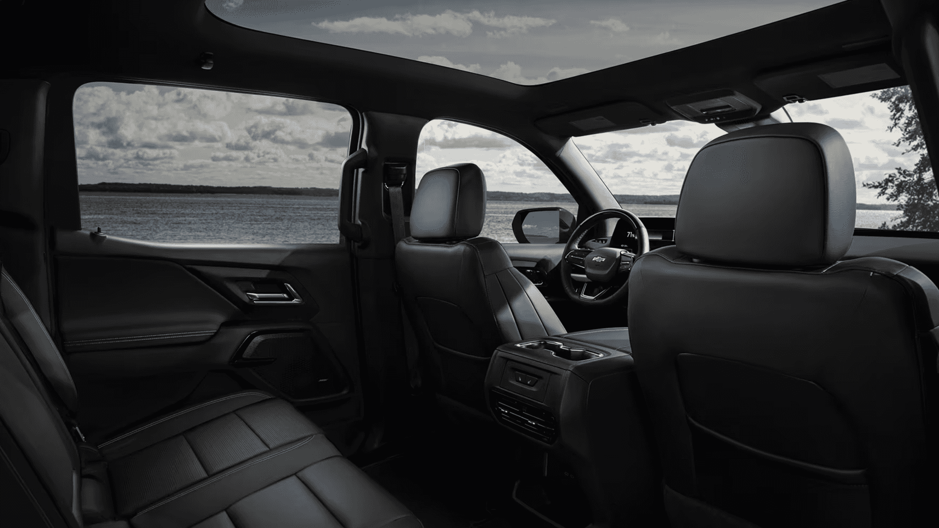 Rear cabin view of 2026 Chevy Silverado EV showing black seats, panoramic glass roof, and lake view