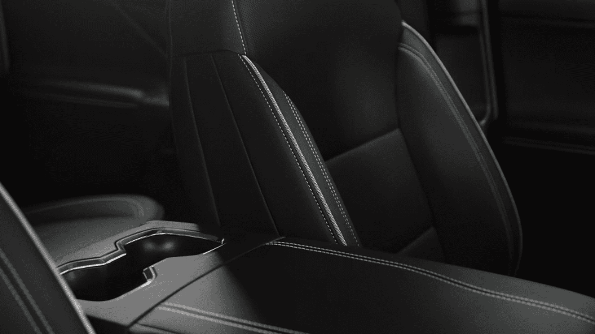 Close-up of Silverado EV front seat with contrast stitching beside center console cupholders and armrest