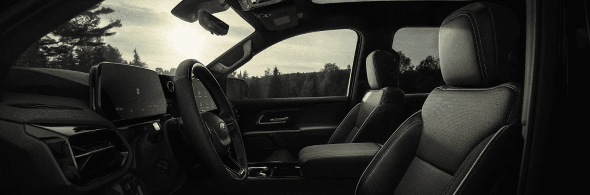 Wide Silverado EV cabin view with dual displays, steering wheel, and front seats under tinted glass