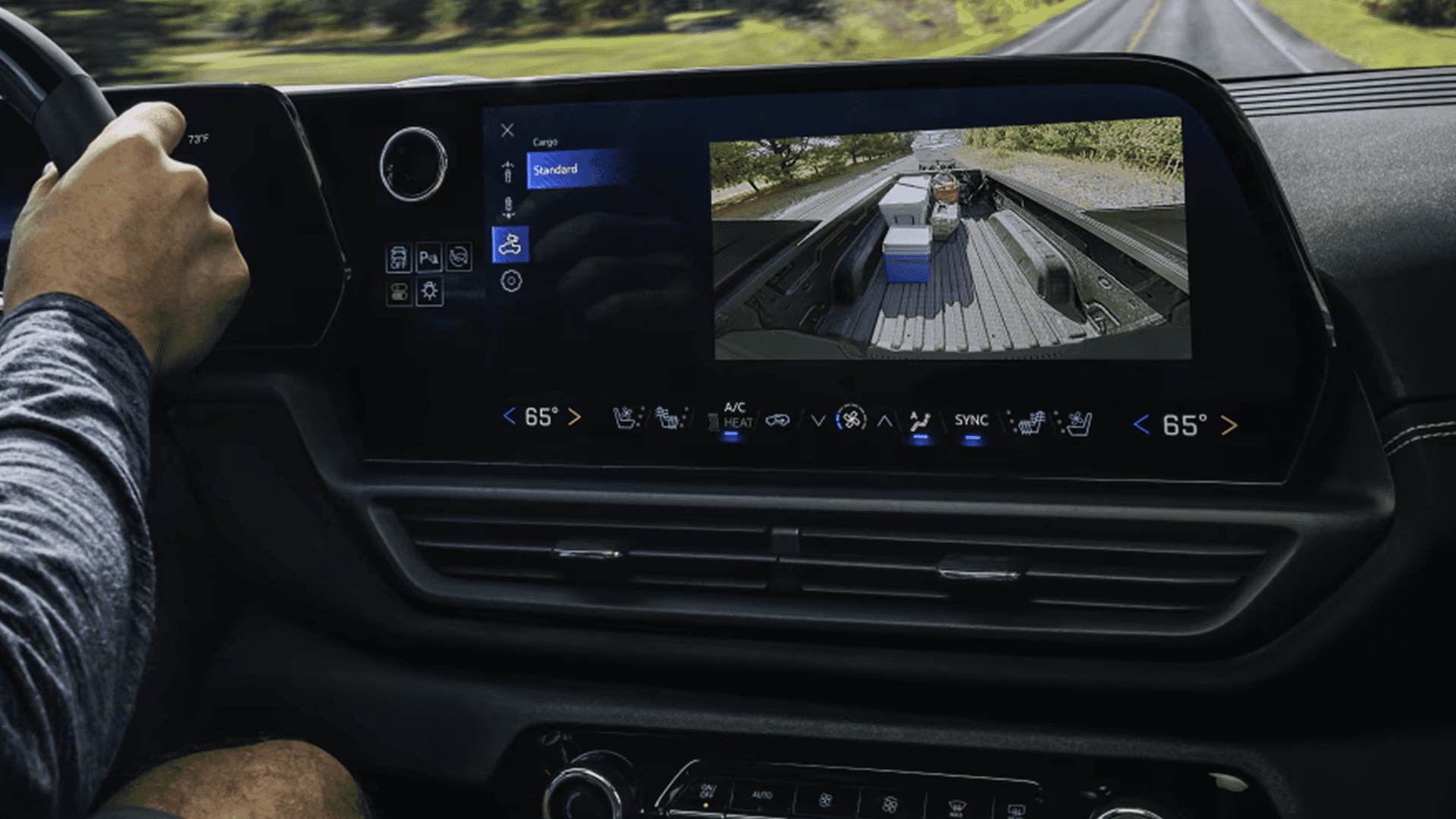 Silverado EV touchscreen shows bed camera view with cargo while driving on a two lane road