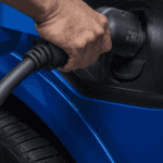 Close-up of hand inserting charging connector into blue Equinox EV charge port near front wheel