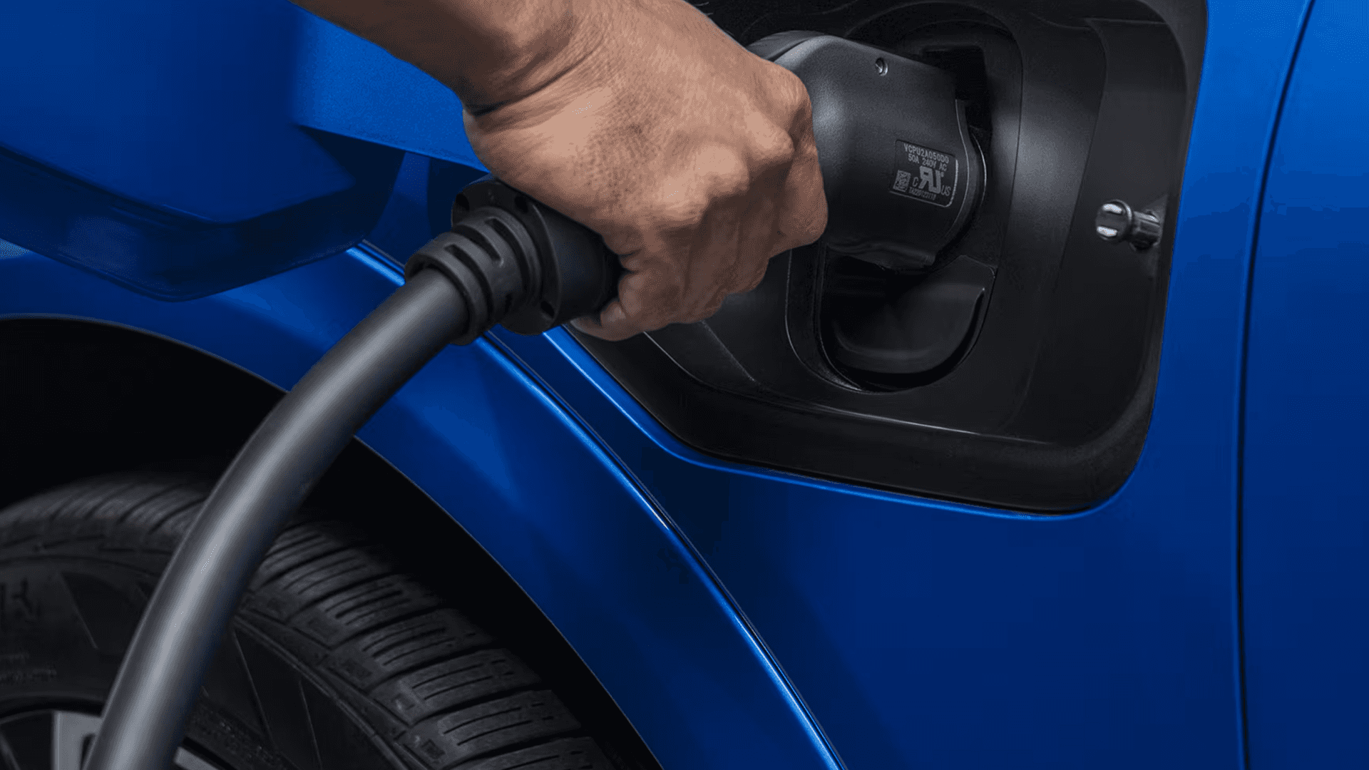 Close up of hand inserting charging connector into blue Equinox EV charge port near front wheel