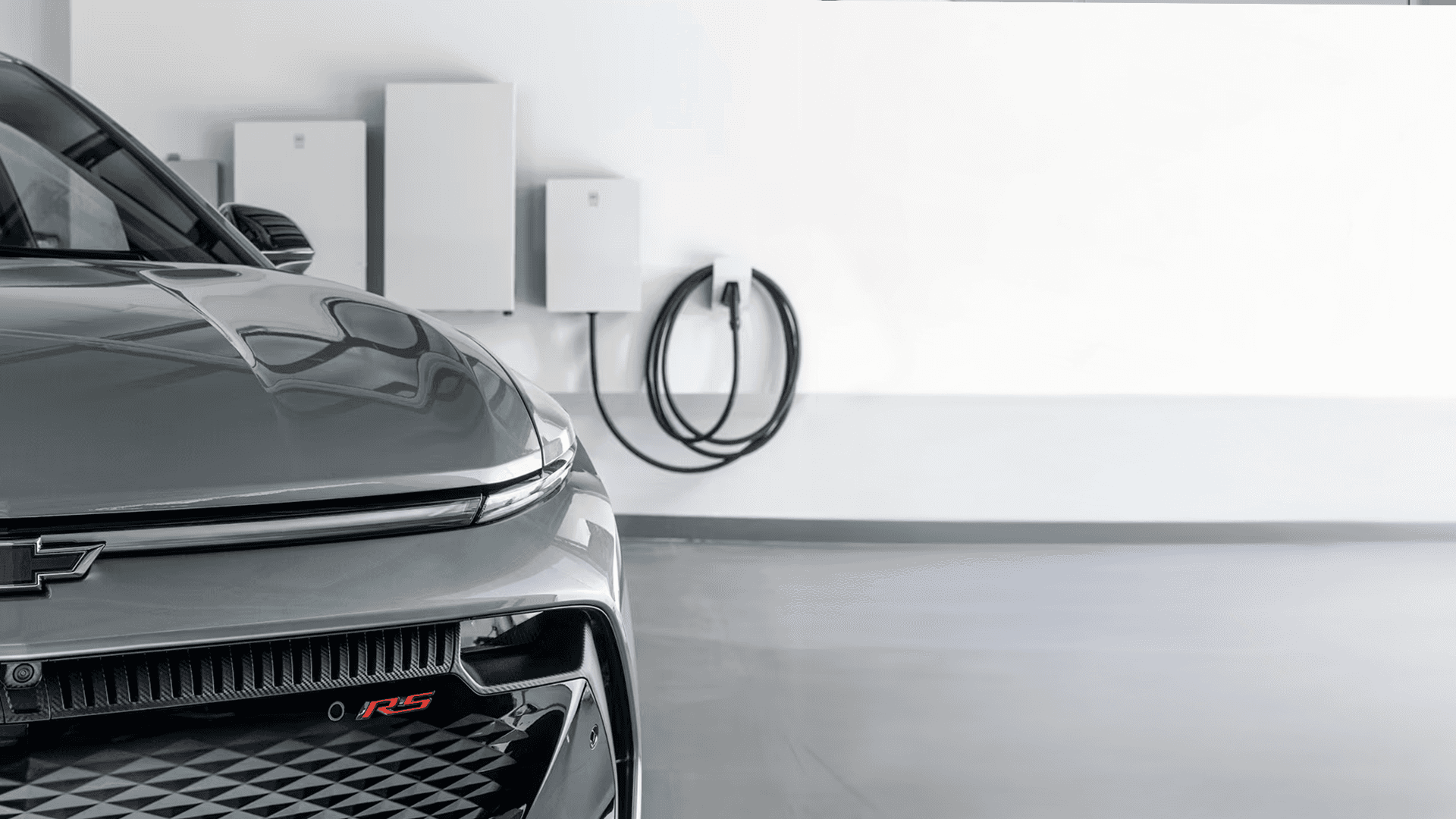 Silver Equinox EV RS charging in garage beside GM Energy wall units and coiled charging cable