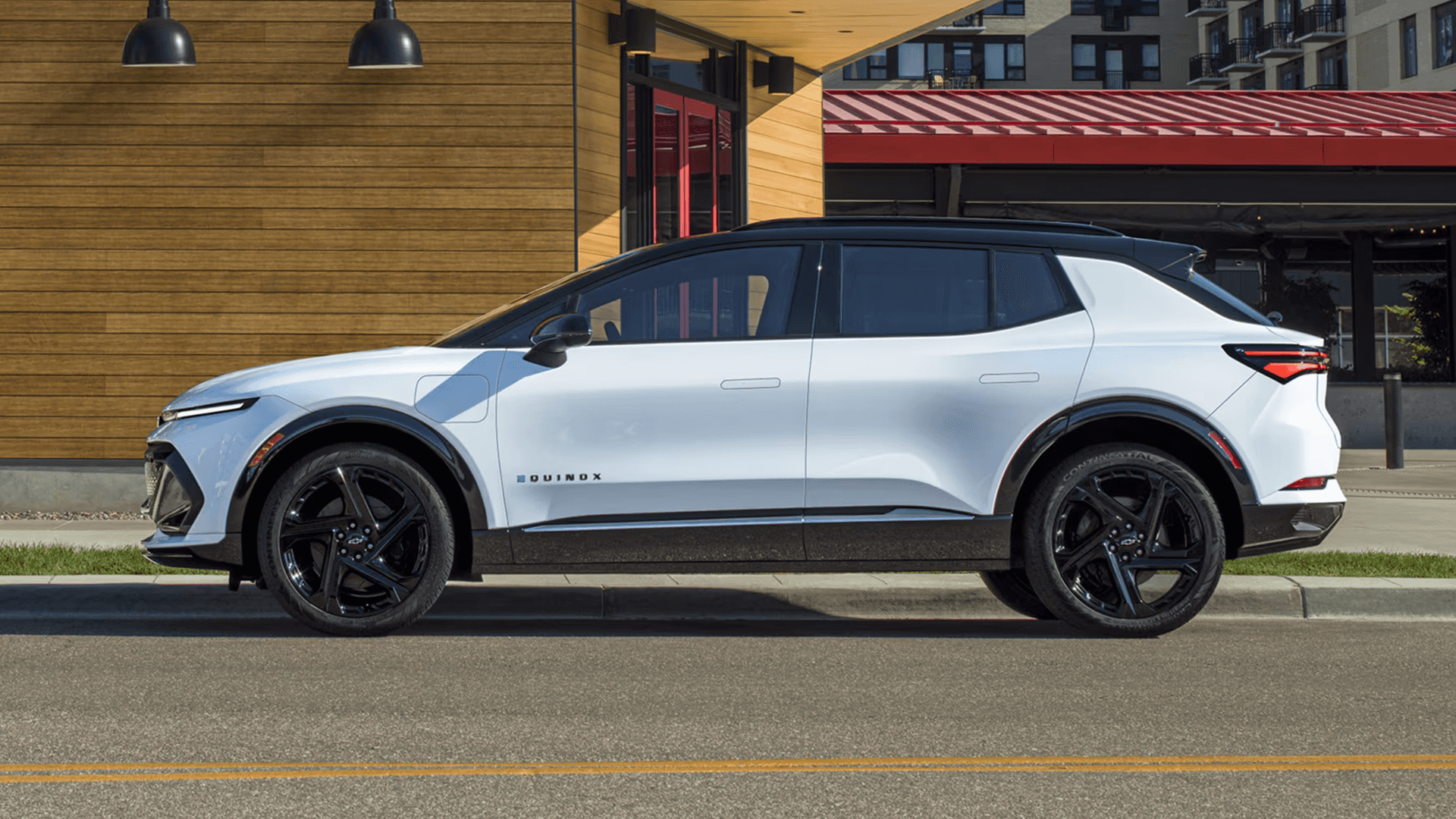 White Chevy Equinox EV parked curbside in an urban setting, showing sleek side profile and black roof.