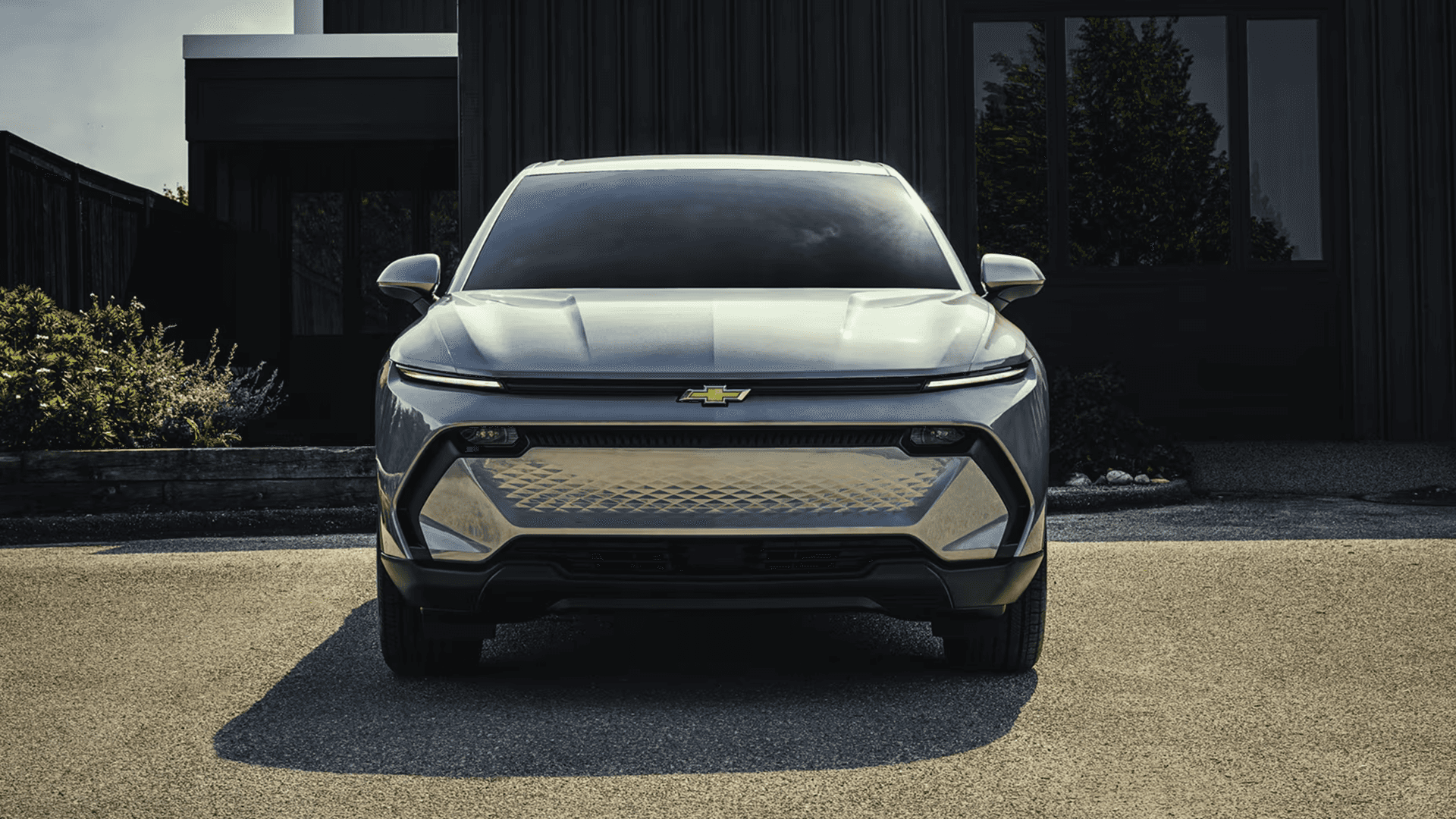 Front view of silver Chevy Equinox EV highlighting full width LED signature lighting and patterned lower grille panel.