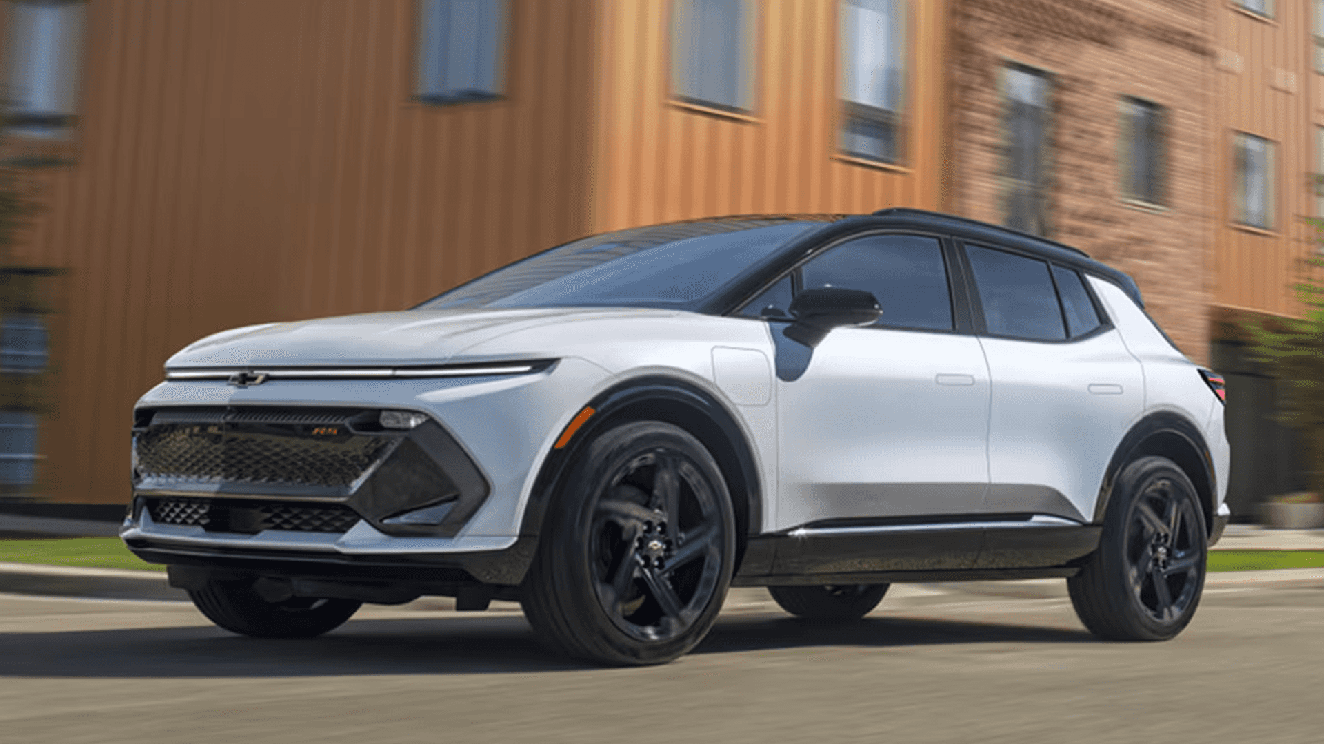 White 2026 Chevy Equinox EV in motion on city street, black roof and wheels, side profile