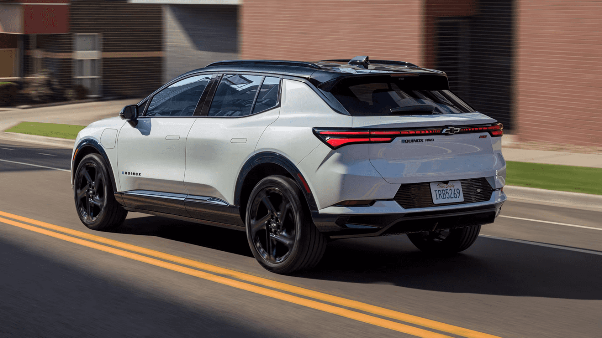 Rear three quarter view of white 2026 Chevy Equinox EV driving on road with full width LED taillights
