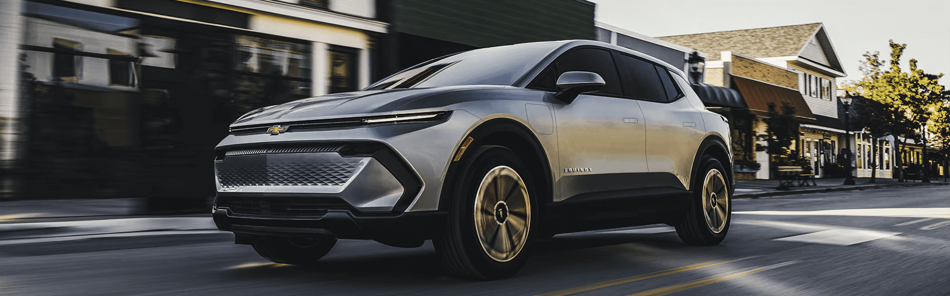 Silver 2026 Chevy Equinox EV driving past small town storefronts, three quarter front view
