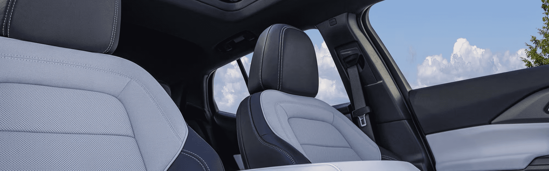 Wide cabin view of two-tone Equinox EV front seats under glass roof with sky visible through side window