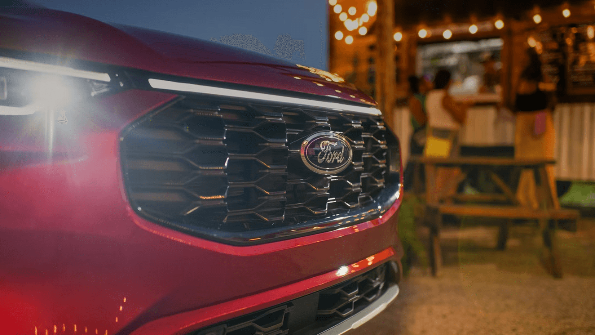 Red 2026 Ford Escape grille and headlamp close-up with LED signature lighting near an outdoor café at night.
