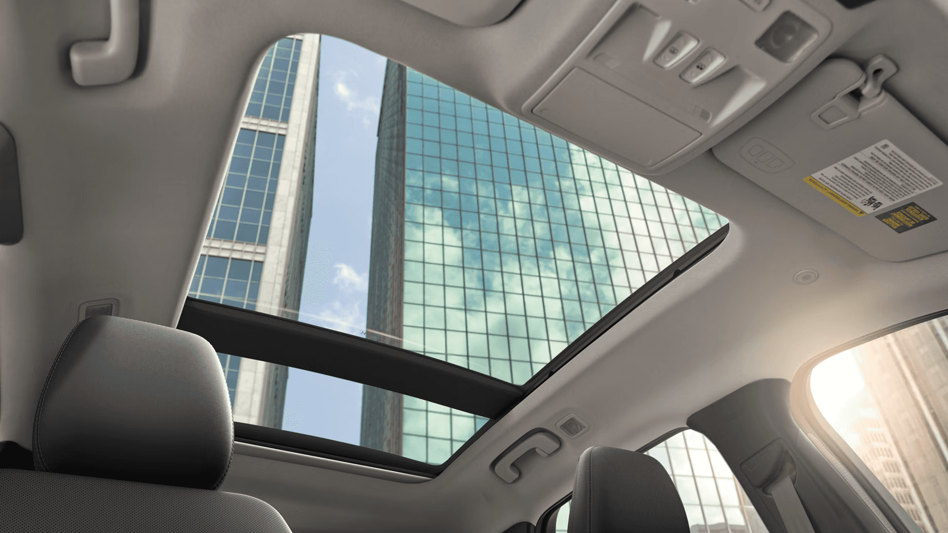 View up through 2026 Ford Escape panoramic roof, showing overhead console and city buildings above