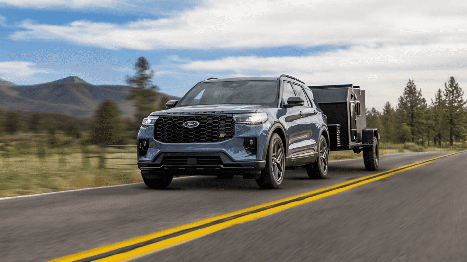 2026 Ford Explorer ST towing a trailer on a scenic highway with mountains in the background