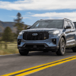 2026 Ford Explorer ST towing a black trailer on an open two-lane road with forest scenery