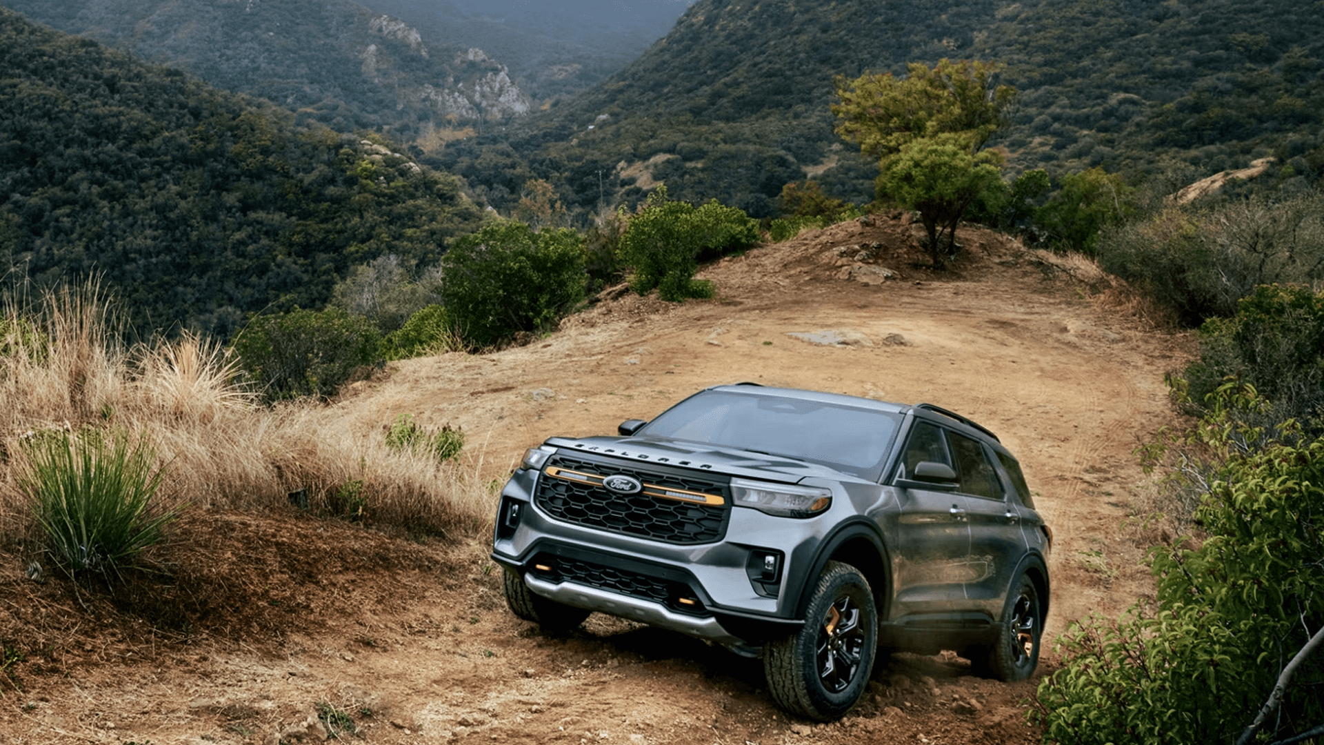 2026 Ford Explorer Tremor climbing a hilltop trail, highlighting rugged stance and off road design details.