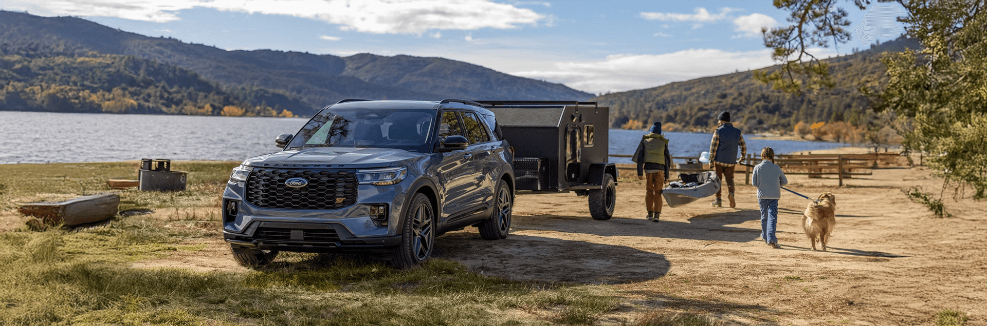 Gray 2026 Ford Explorer ST parked near a lake with trailer, showcasing bold grille and sporty styling.