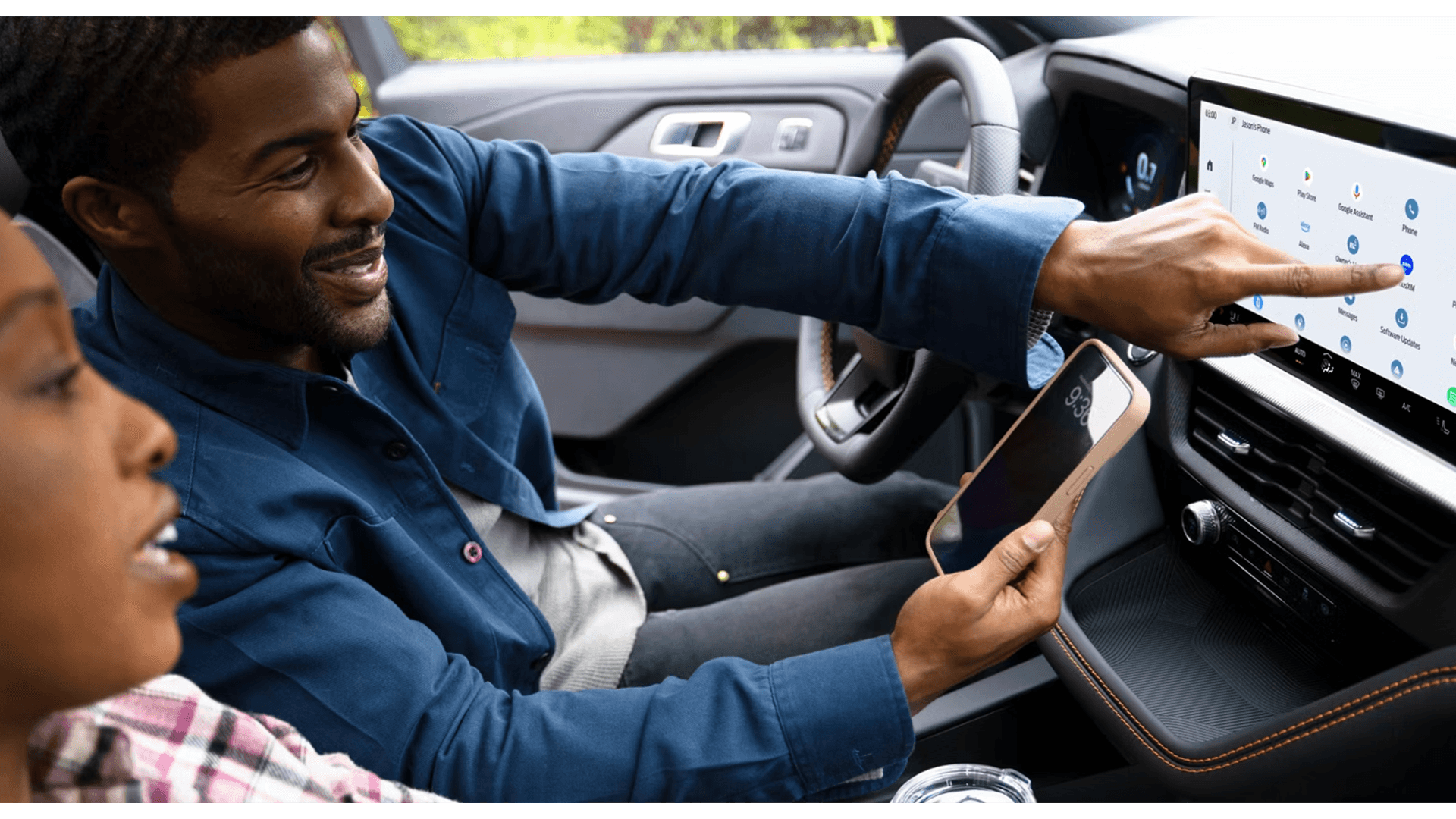 Driver pointing at 2026 Ford Explorer touchscreen while holding phone, demonstrating connected features