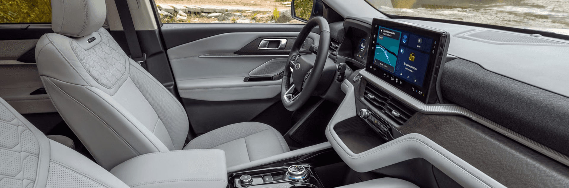 Front cabin view of 2026 Ford Explorer with light gray seats, wide touchscreen, and rotary dial shifter
