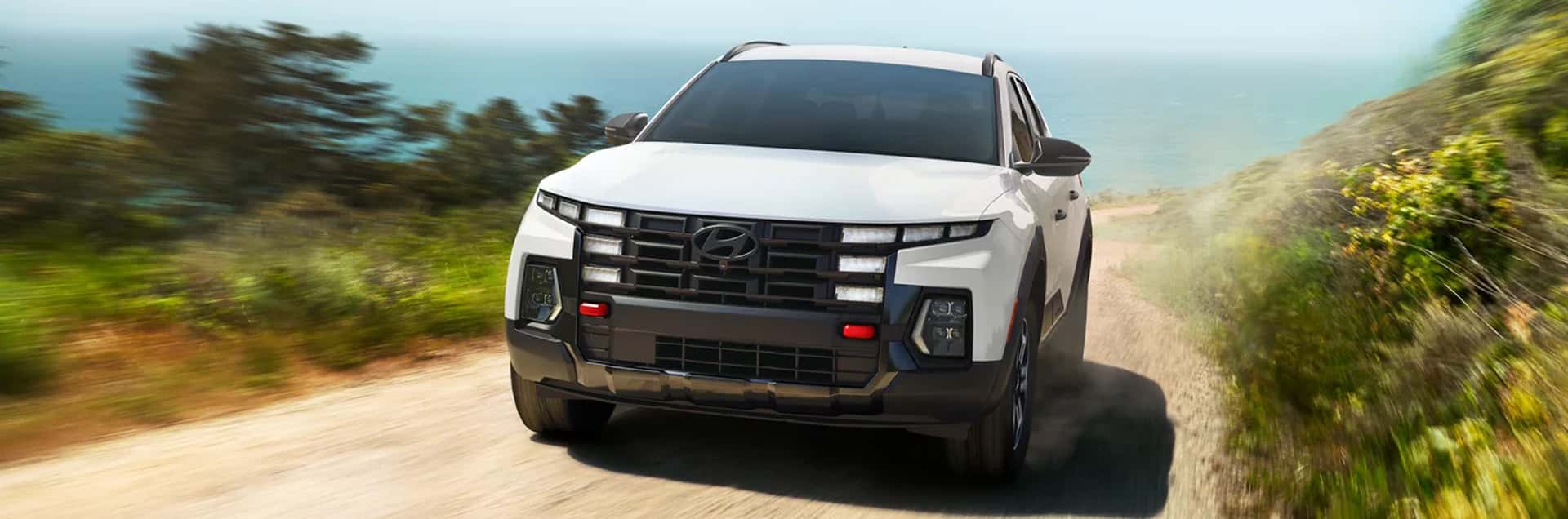 2026 Hyundai Santa Cruz driving on a coastal dirt road, showing rugged front design and compact pickup styling