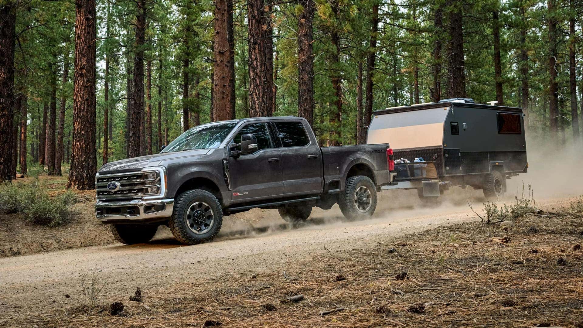 2026 Ford F-250 Super Duty towing an off-road camper trailer on a forest trail demonstrating heavy-duty capability