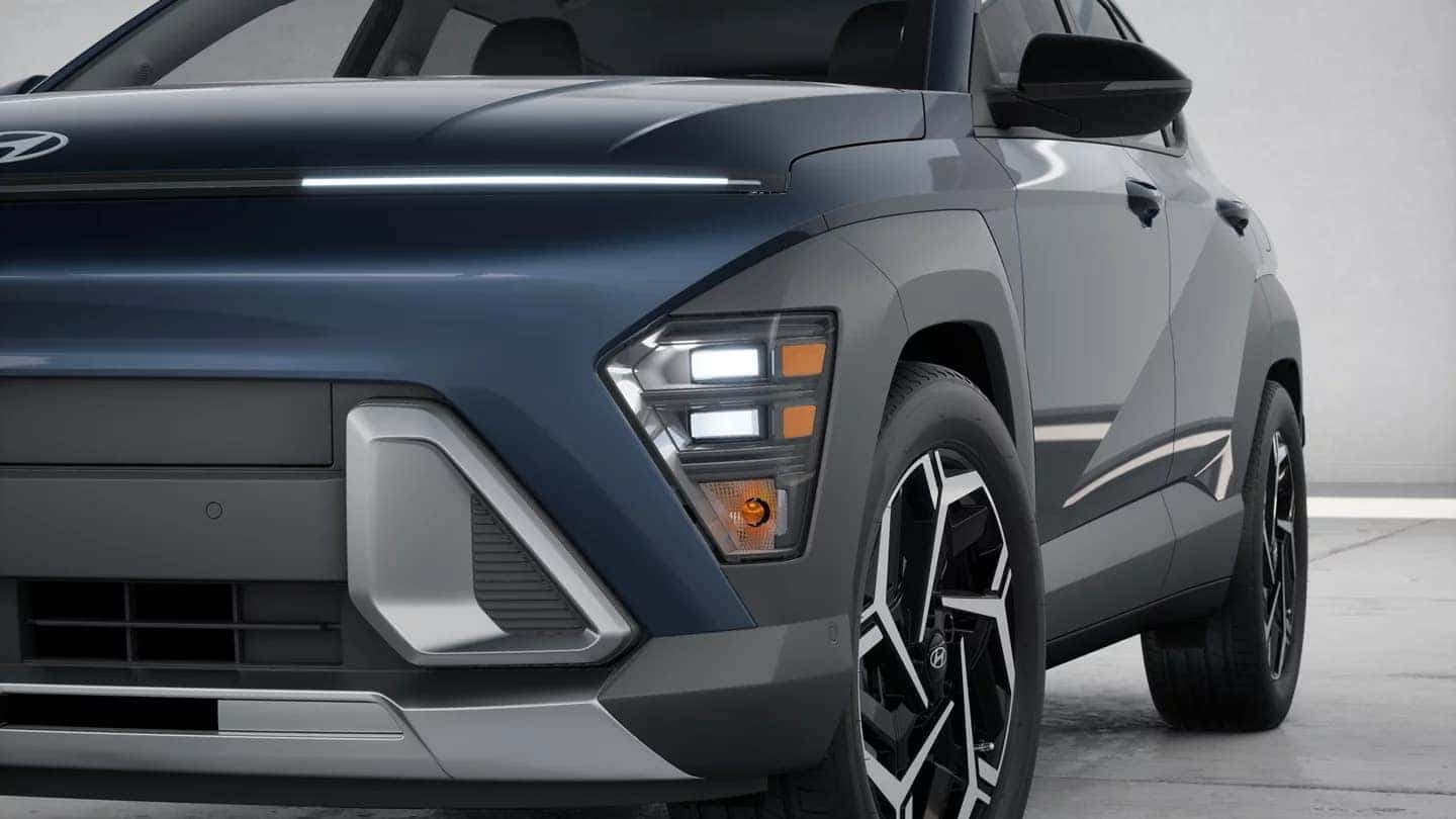 Close up front view of a gray 2026 Hyundai Kona showing LED daytime running lights, front bumper design, and sculpted grille details.