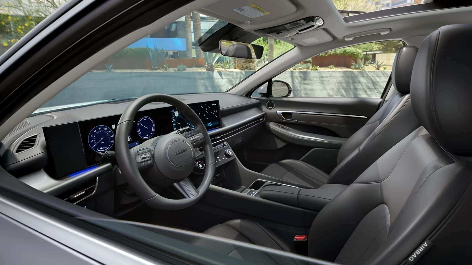 Driver perspective of the 2026 Hyundai Sonata interior featuring the digital instrument cluster, wide infotainment screen, steering wheel controls, and center climate panel.