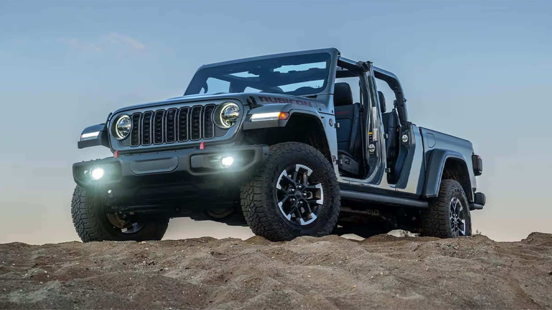 Front three-quarter view of a 2026 Jeep Gladiator Rubicon showing seven-slot grille, round headlights, and fog lights.