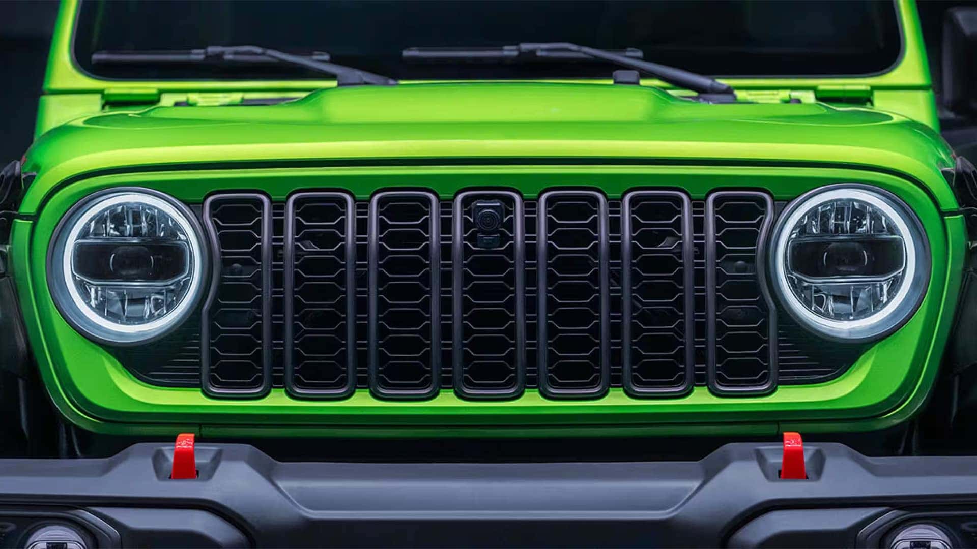 Close-up of the 2026 Jeep Wrangler front showing seven-slot grille, round LED headlights, and tow hooks.