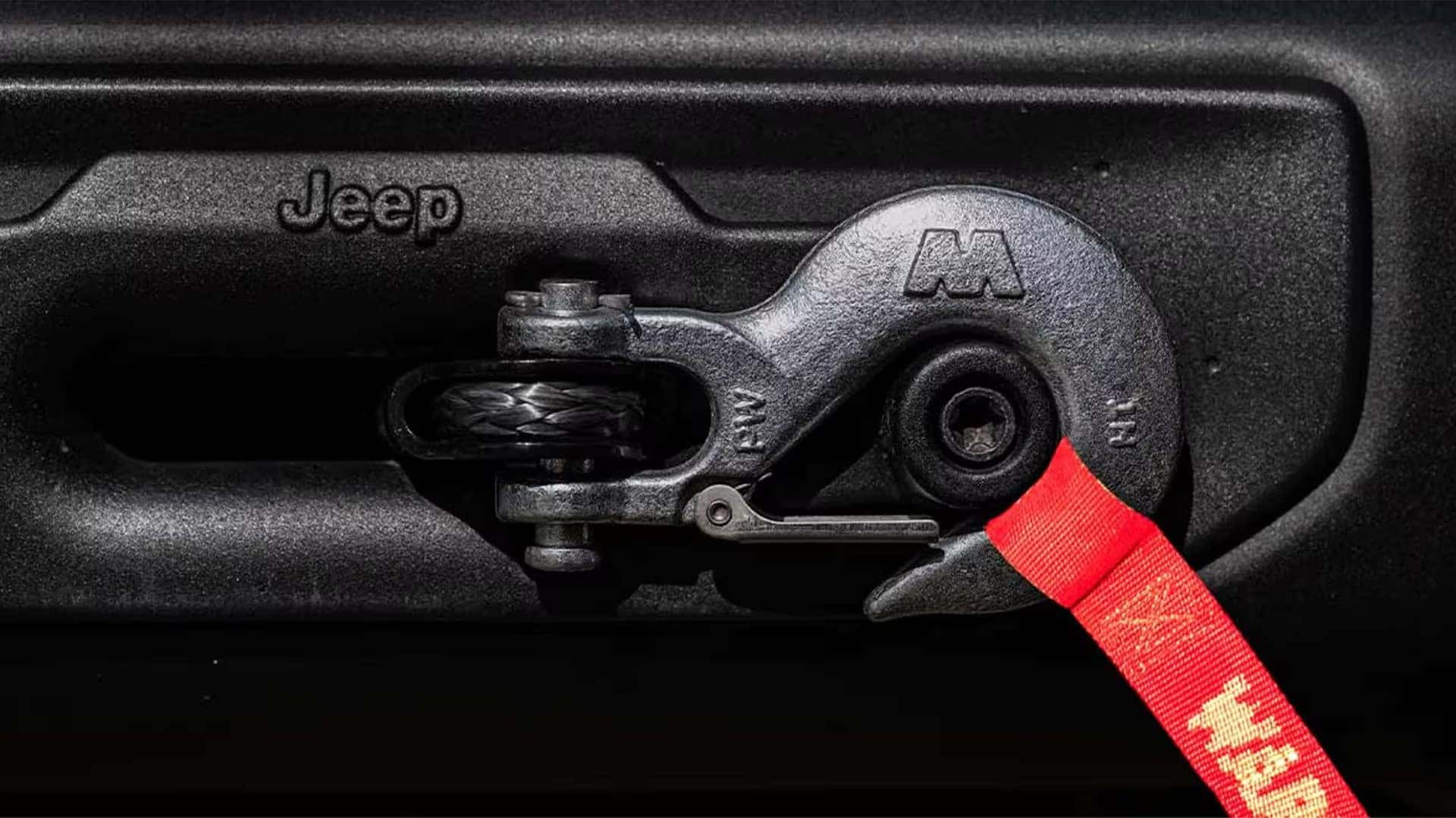 Close-up of 2026 Jeep Wrangler front tow hook and recovery shackle with red strap attached