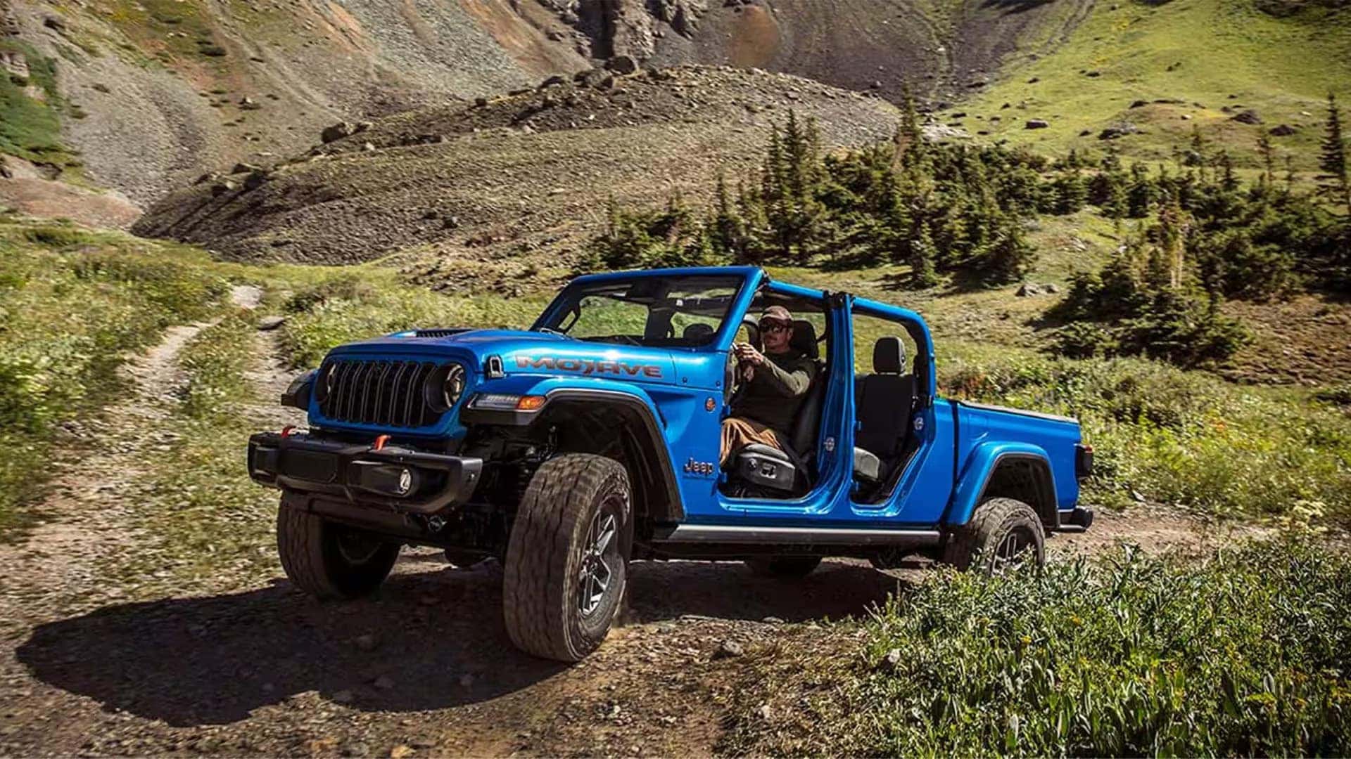 Blue 2026 Jeep Gladiator Mojave on a mountain trail with doors removed, highlighting open-air design and off-road stance.