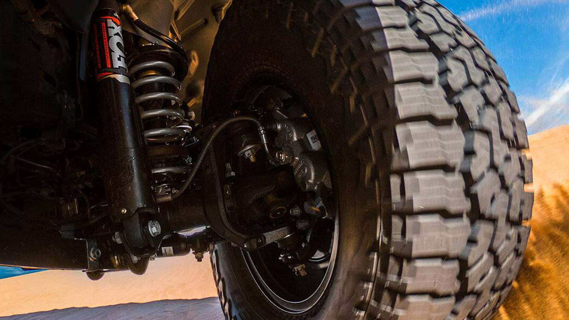 Close-up of 2026 Jeep Gladiator suspension and all-terrain tire on sand, highlighting off-road hardware