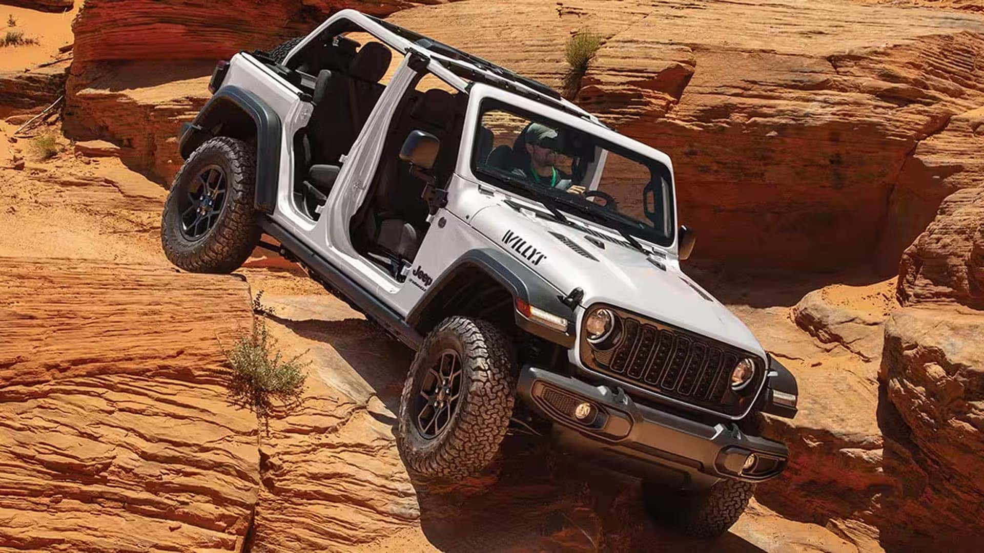 White 2026 Jeep Wrangler Willys navigating steep sandstone terrain with open-air doors removed