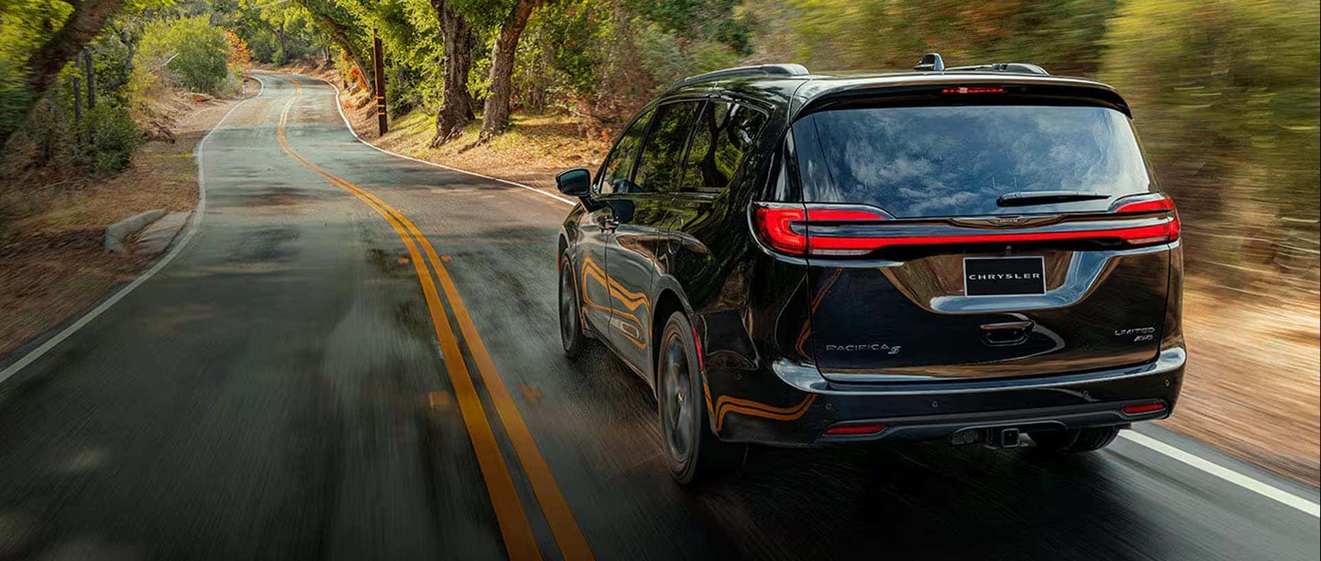 Rear view of 2026 Chrysler Pacifica driving on a winding road with LED taillight light bar and liftgate design