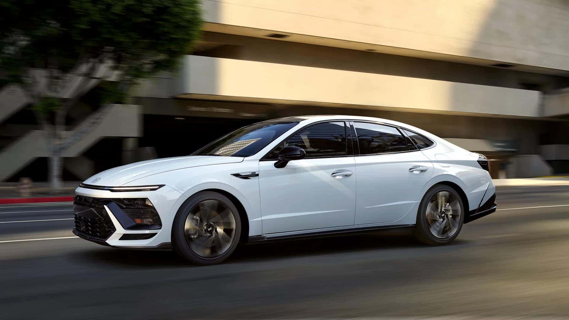 Side profile of a 2026 Hyundai Sonata driving on a city street, emphasizing smooth handling, sporty stance, and confident midsize sedan performance