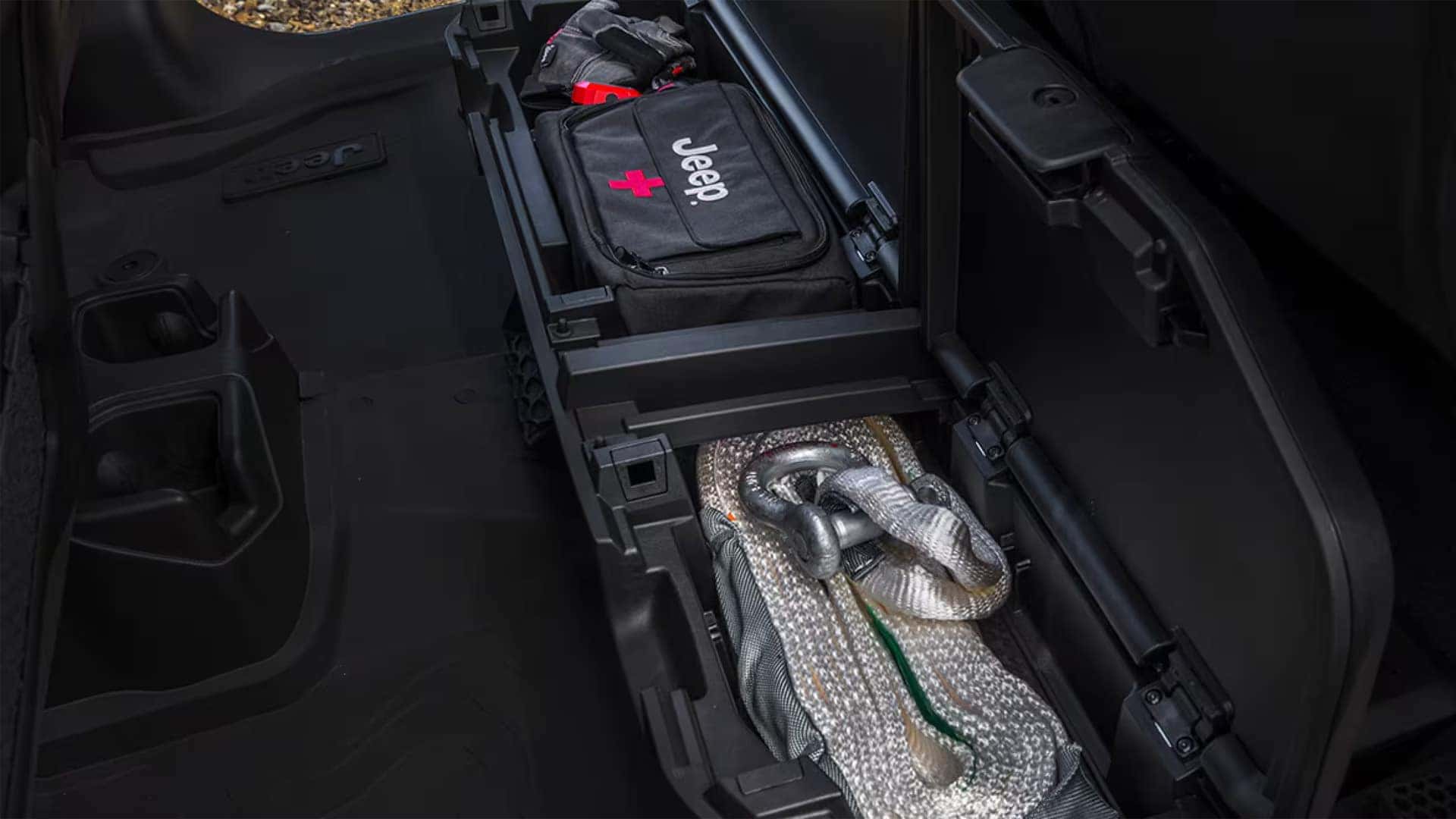 Under rear seat storage in the 2026 Jeep Gladiator interior with lockable bin holding gear and recovery strap