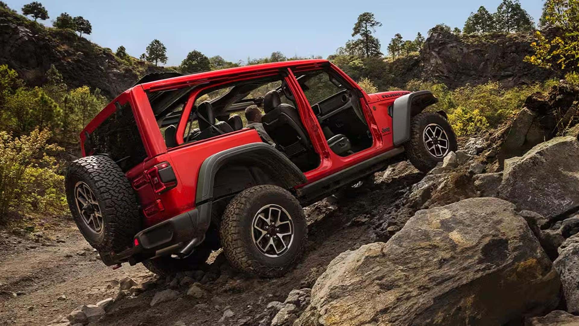 Red 2026 Jeep Wrangler climbing over large rocks with doors removed, demonstrating Trail Rated off-road capability