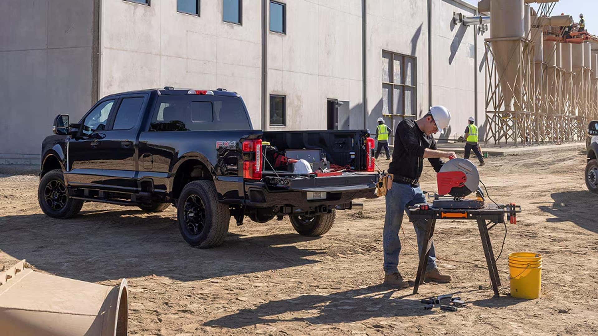 Black 2026 Ford F-250 Super Duty with tailgate open at jobsite, showing truck bed workspace and rear LED taillights.