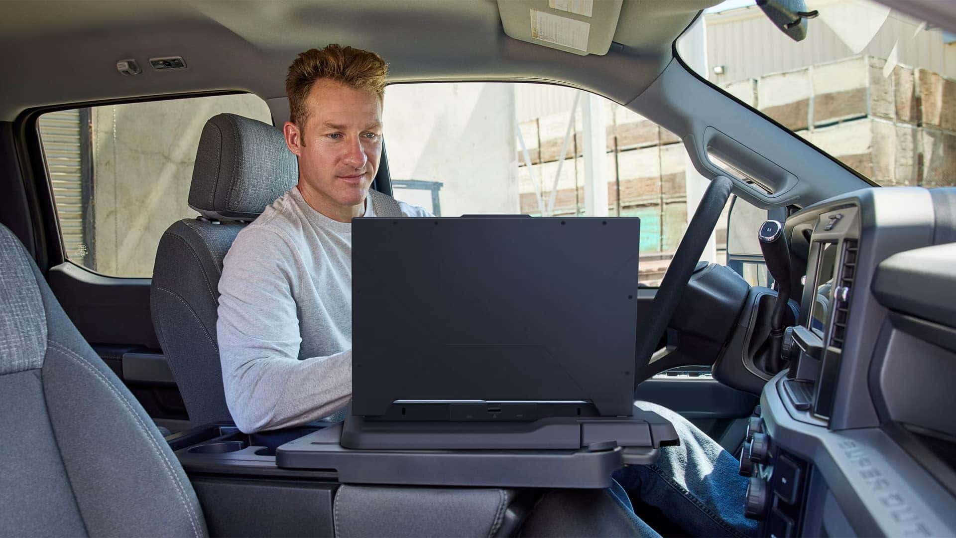 Driver using the available interior work surface in the 2026 Ford F-250 Super Duty with a laptop, highlighting mobile office functionality and productivity features