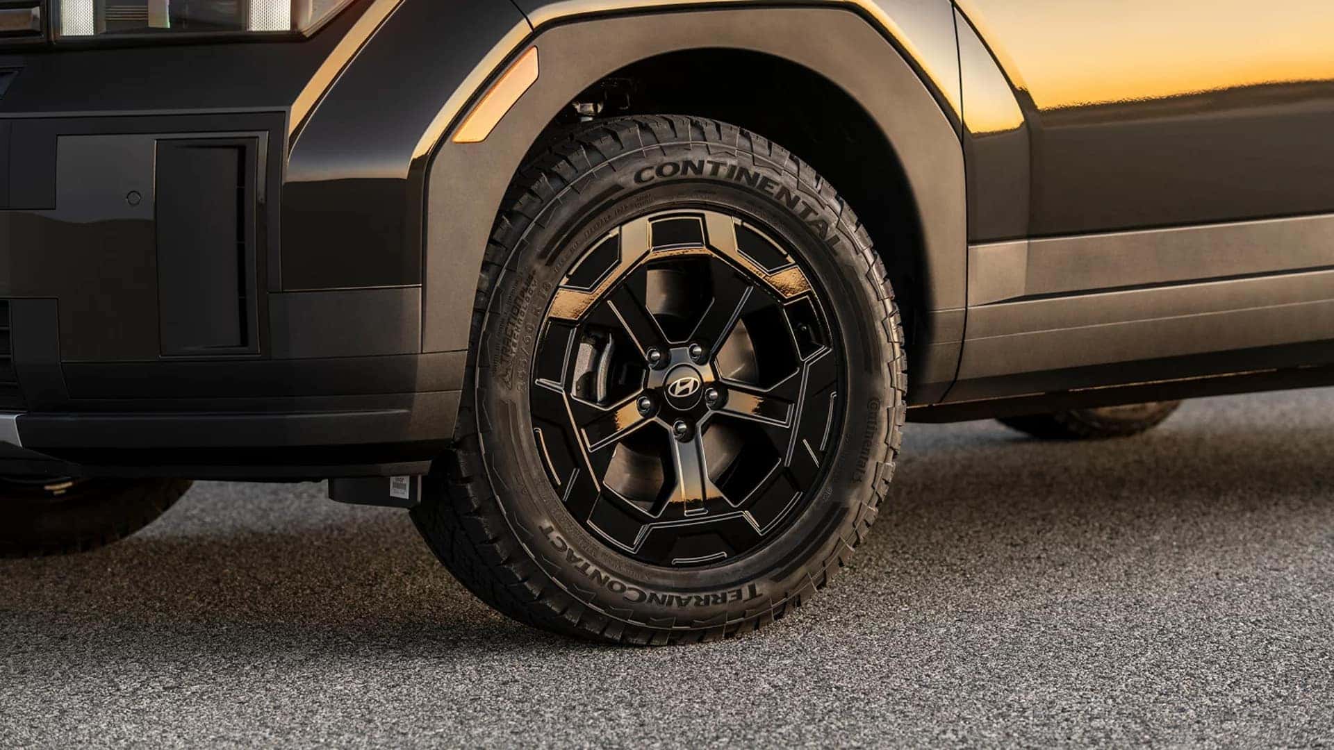 Close-up of a 2026 Hyundai Santa Fe wheel with black alloy rim, all-season tire, and rugged fender cladding.