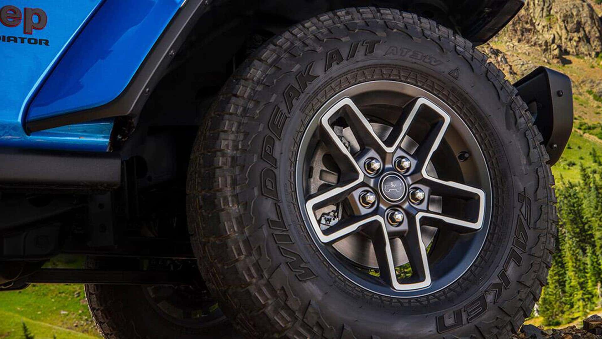 Close-up of a 2026 Jeep Gladiator wheel and Falken Wildpeak all-terrain tire on a blue truck with rugged fender flare.