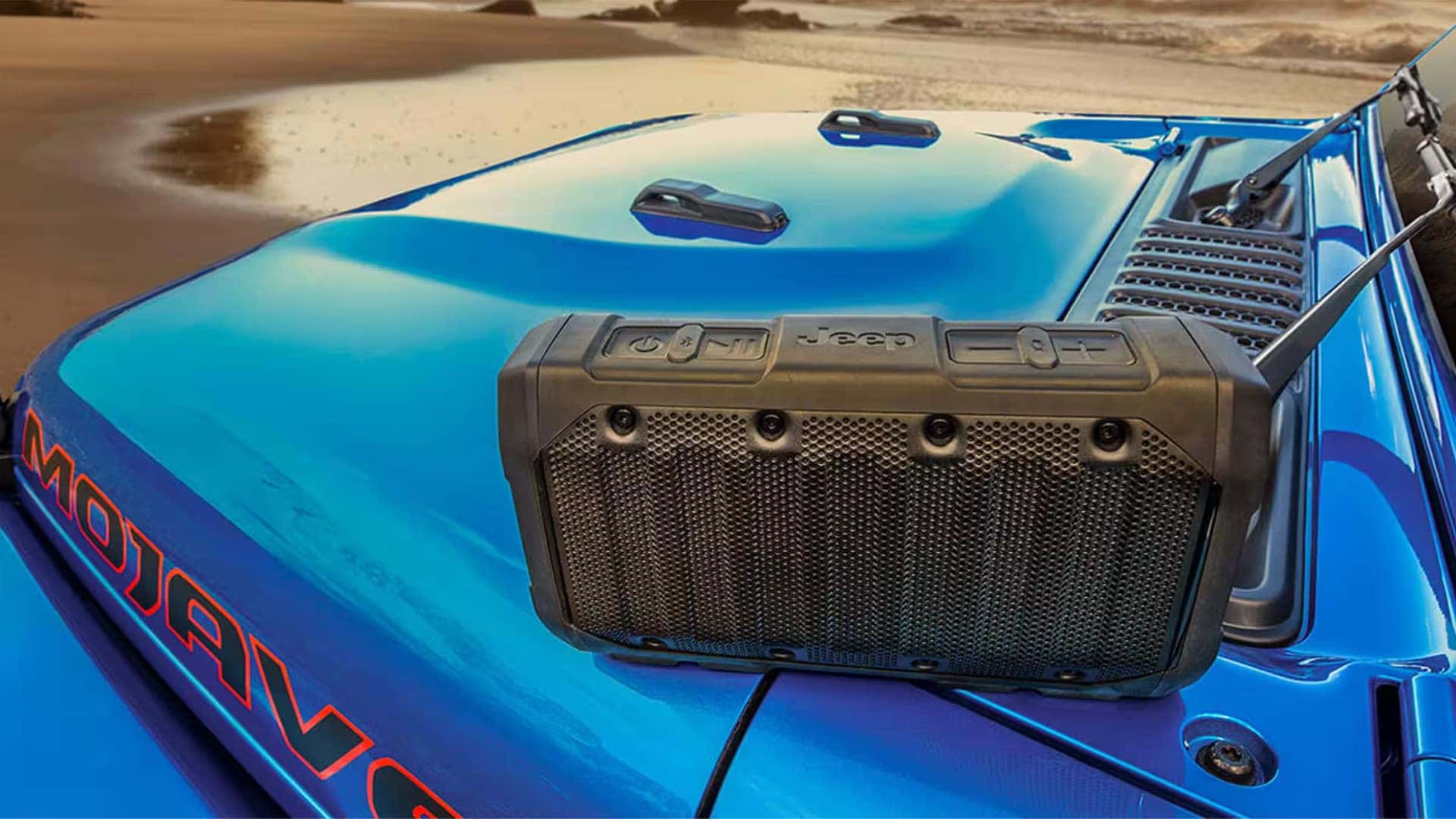 Jeep removable Bluetooth speaker on the hood of a blue 2026 Jeep Gladiator near the beach