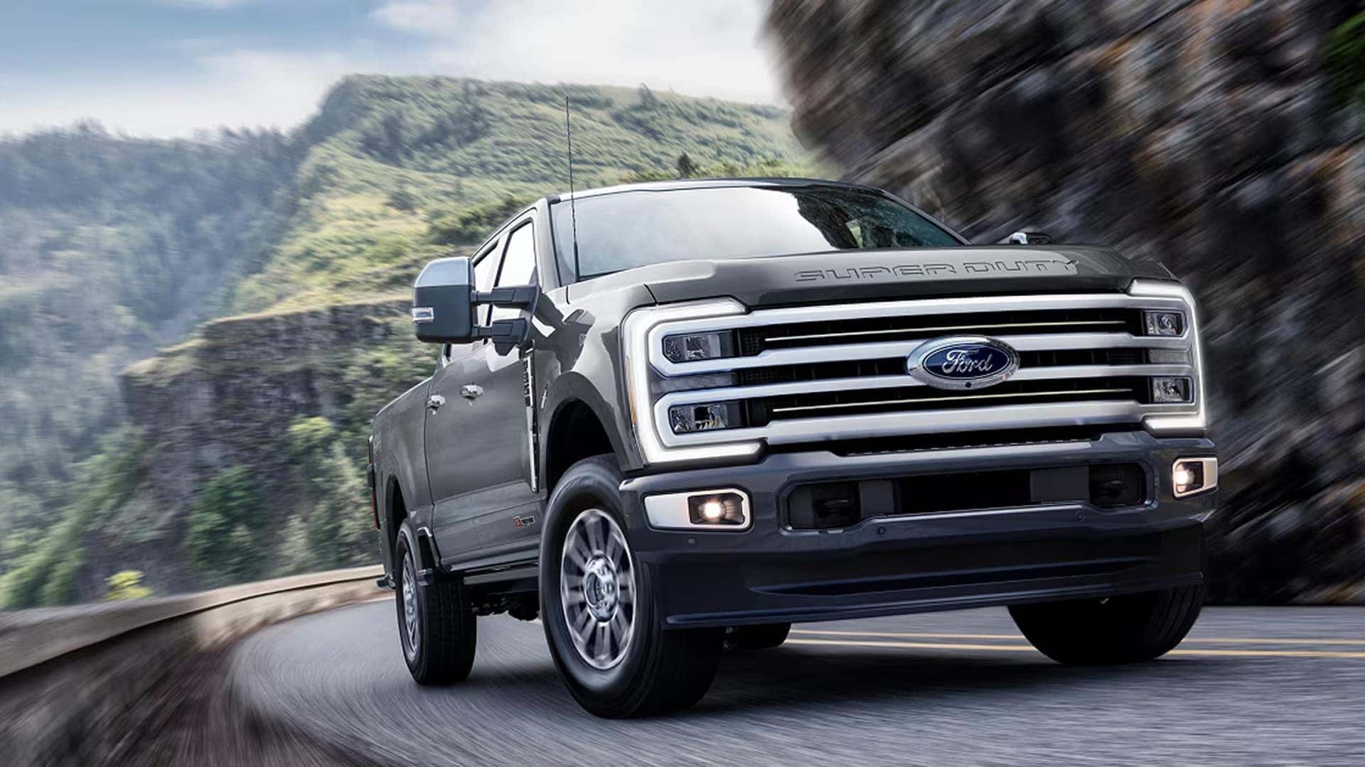 2026 Ford F-250 Super Duty driving on a winding mountain road, showcasing powerful front grille design, LED lighting, and confident heavy-duty performance