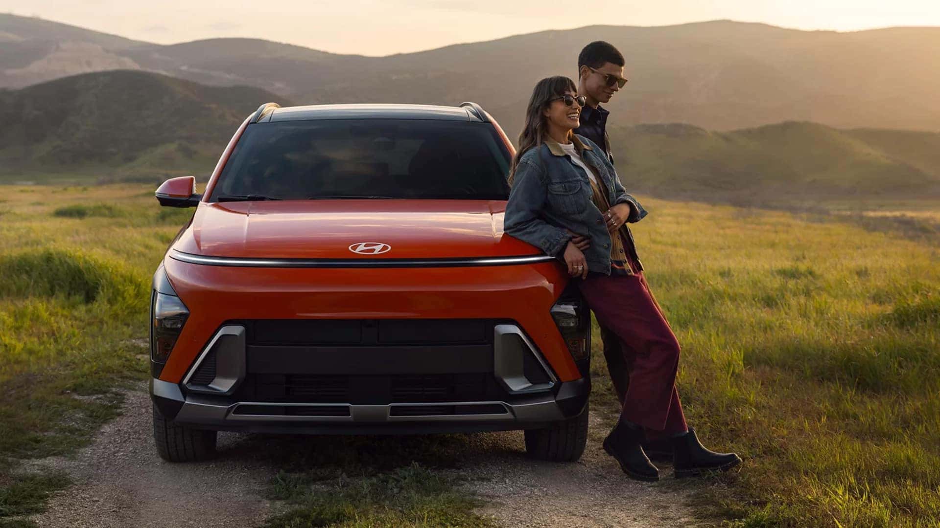 Rear view of a 2026 Hyundai Kona driving through a mountain landscape, highlighting exterior dimensions, rear lighting design, and road presence