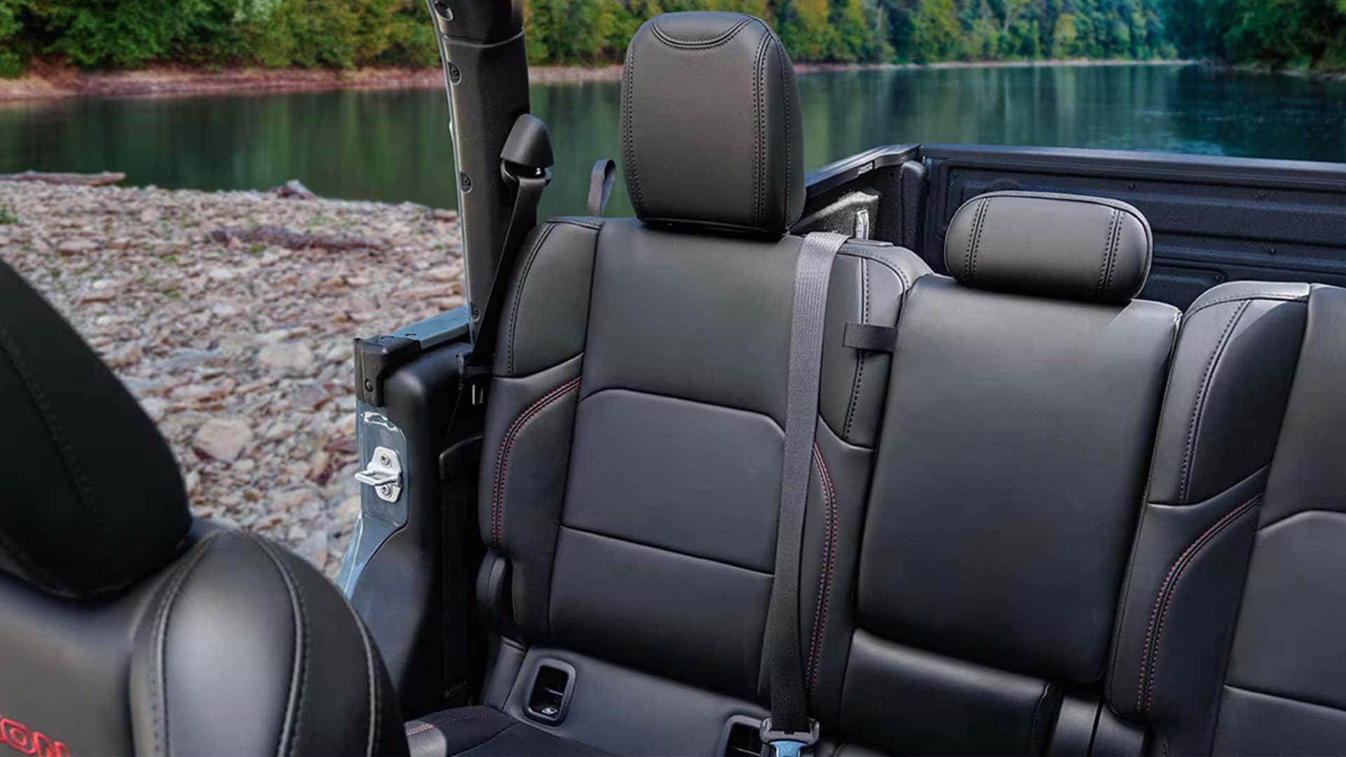 2026 Jeep Gladiator rear seat bench with headrests and seatbelt, shown in open-air cabin by a lake