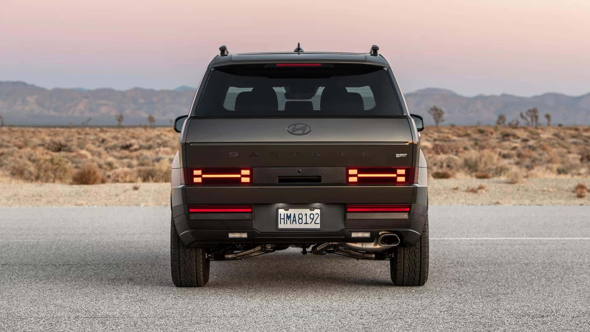 Rear view of a 2026 Hyundai Santa Fe showing trim specific badging, horizontal LED tail lights, and wide stance on an open road