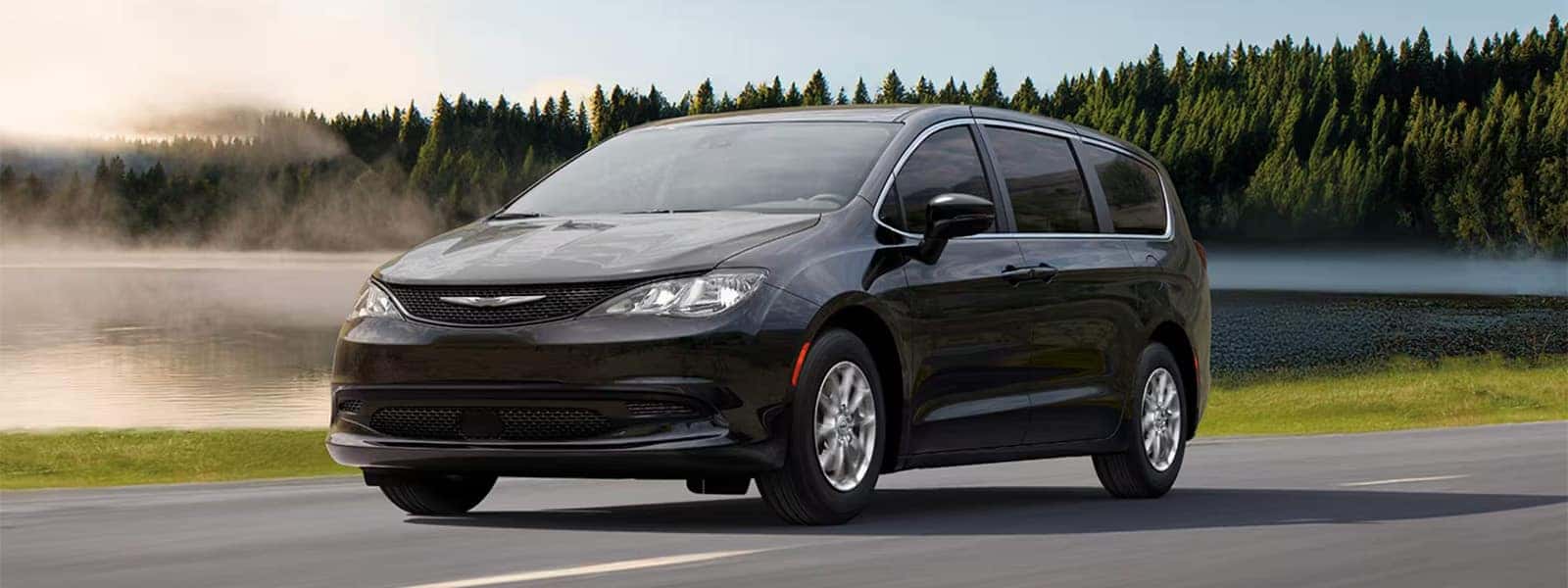 2026 Chrysler Voyager driving on a scenic road with trees and water in the background