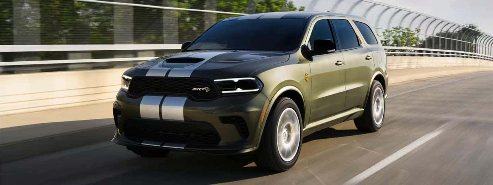 2026 Dodge Durango SRT Hellcat performance SUV driving on a highway bridge, front three quarter view showing hood scoop, LED headlights, and bold muscle SUV styling