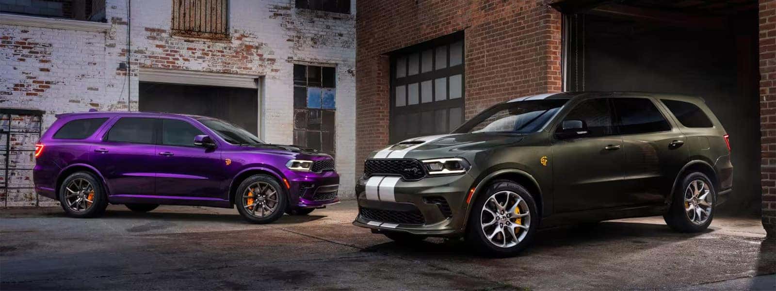 2026 Dodge Durango trim lineup with purple and green performance SUVs parked outside an industrial brick garage