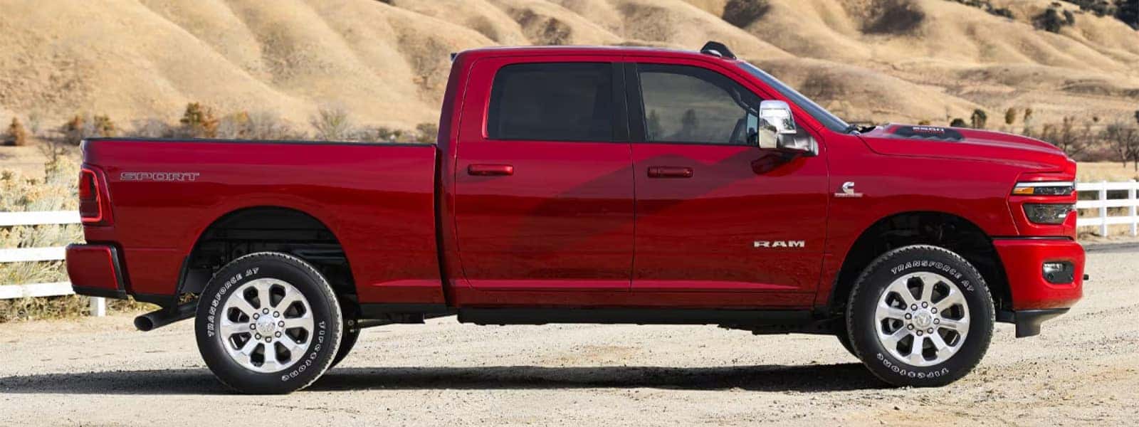 Red 2026 RAM 2500 heavy duty pickup truck in side profile parked on a rural road with hills in the background